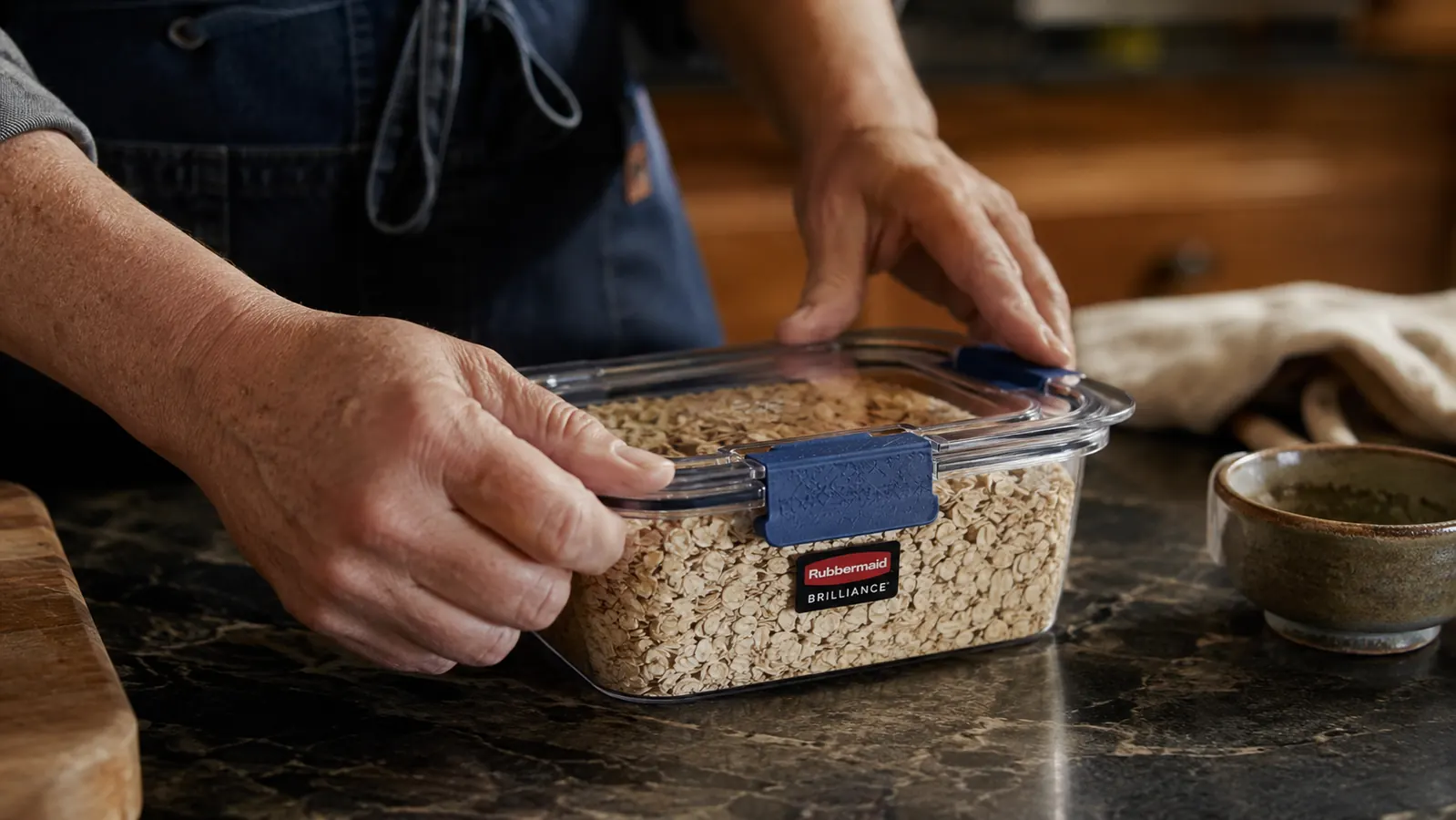 A hand latching down the lid on a clear food storage container filled with bulk-bought oats