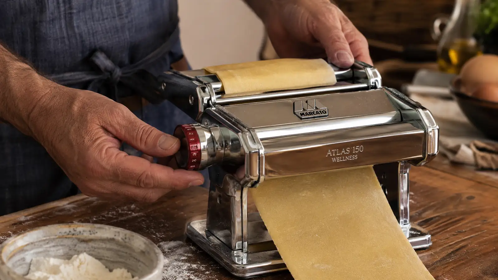 A hand adjusting the thickness dial on the Marcato Atlas pasta machine before feeding dough through